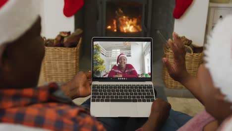 una pareja afroamericana agitando y usando una computadora portátil para una videollamada de navidad con una mujer en la pantalla