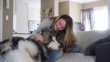 mujer acurrucando a su perro husky en un sofá