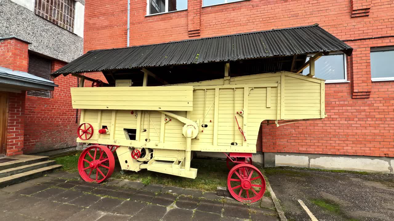 A Vintage Threshing Machine Positioned Outdoors Beside a Red-brick Building - Medium Shot