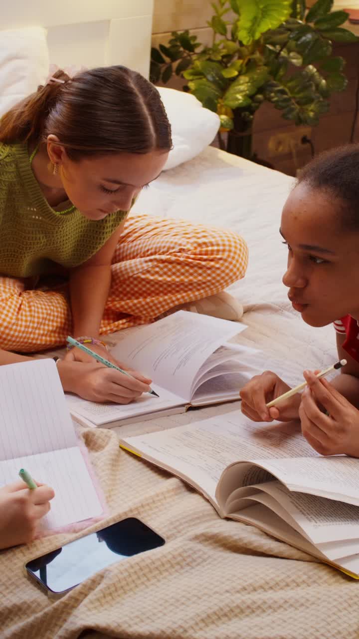 Teenage girls studying together on a bed