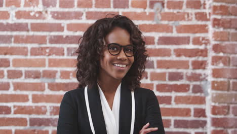 portrait of smiling businesswoman wearing glasses standing against brick wall in modern office