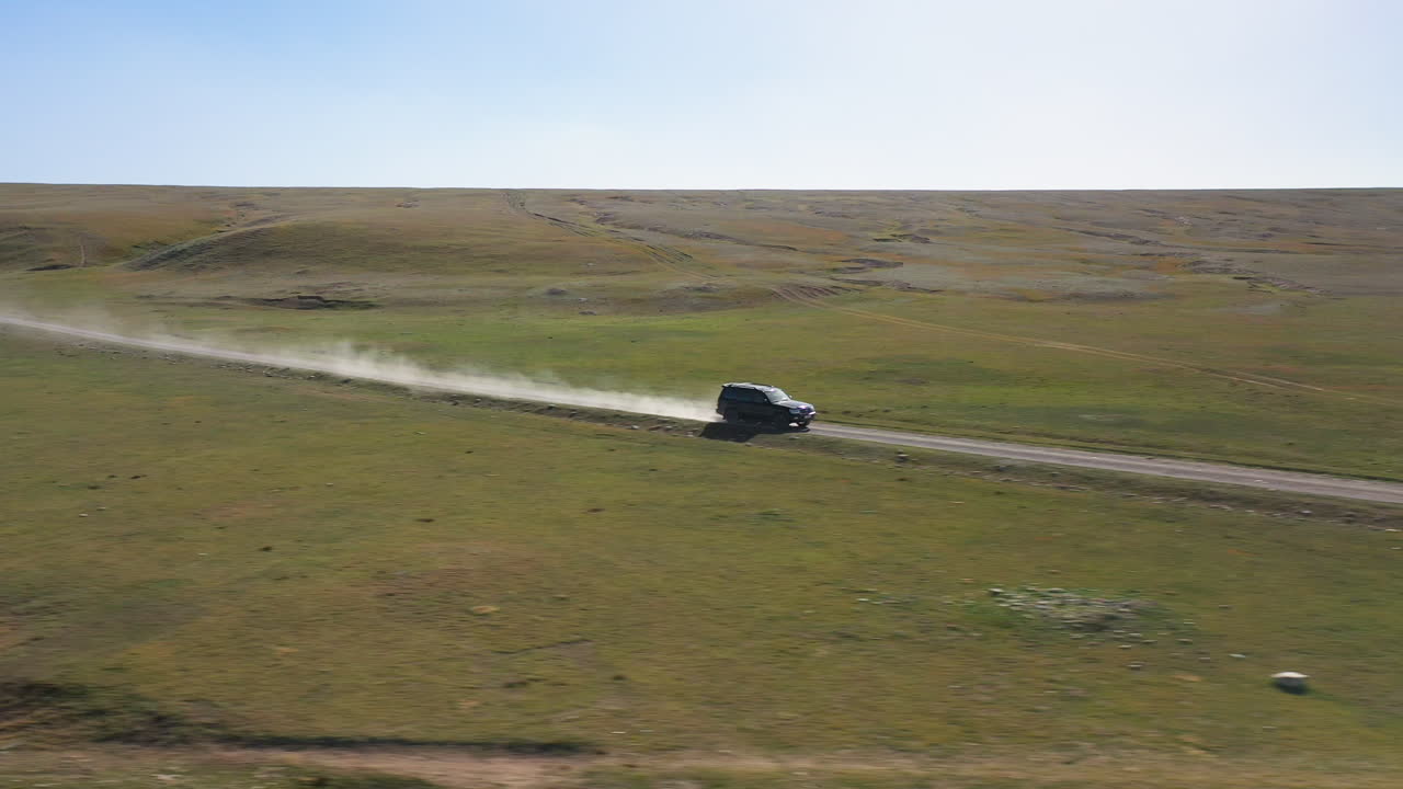 키르기스스탄의 켈수 호수 근처 도로를 따라 suv 뒤에서 먼지를 걷어차는 서사시적인 영화 드론 샷