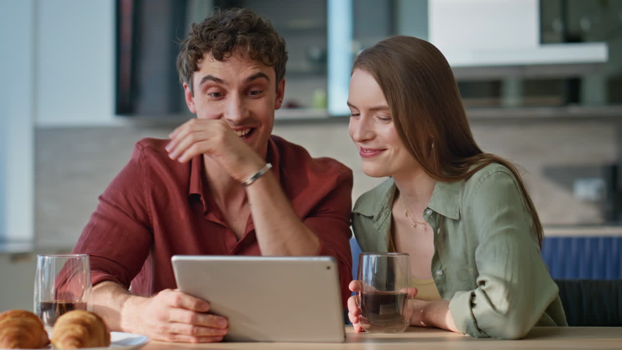 Pair watching tablet video holding coffee cups closeup. Smiling family couple
