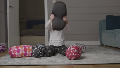 young girl playing around with cushions on floor and throwing them behind her back