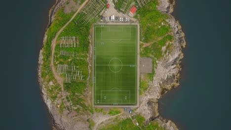 top-down aerial ascent over henningsvaer football pitch on rocky island, lofoten