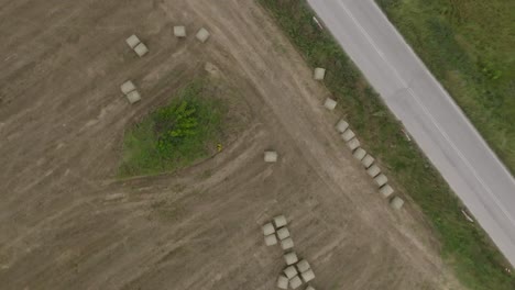 Twisting-aerial-riser-above-farm-land-with-round-hay-bales-next-to-country-road