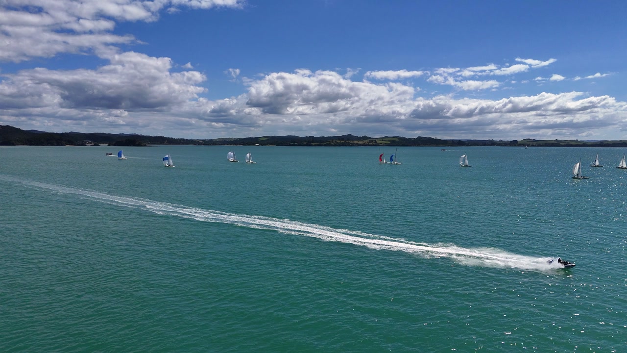 Low aerial: Jet ski and sailboats on sparkling sea water on sunny day