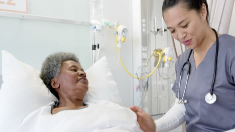 Diverse-female-doctor-talking-with-senior-female-patient-in-hospital-room,-slow-motion