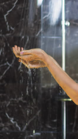 young blonde woman in black bikini holds hands under hot falling water jets in shower cabin against dark marble tile daily routine slow motion