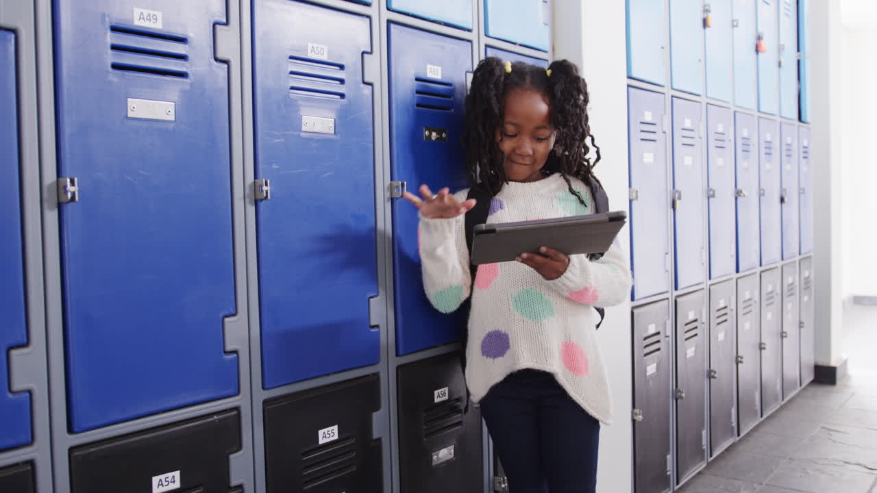 In school hallway, young girl using tablet, smiling near lockers, copy space