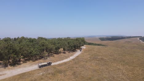 Soldaten-Der-Israelischen-Armee-Auf-Fahrzeugen,-Die-Auf-Der-Landstraße-Des-Übungsgeländes-Durch-Die-Grüne-Wiese-Fahren,-Kamerafahrt-Aus-Der-Luft