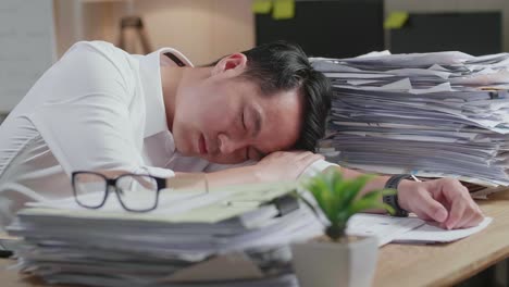 close up of tired asian man sleeping due to working hard with documents at the office