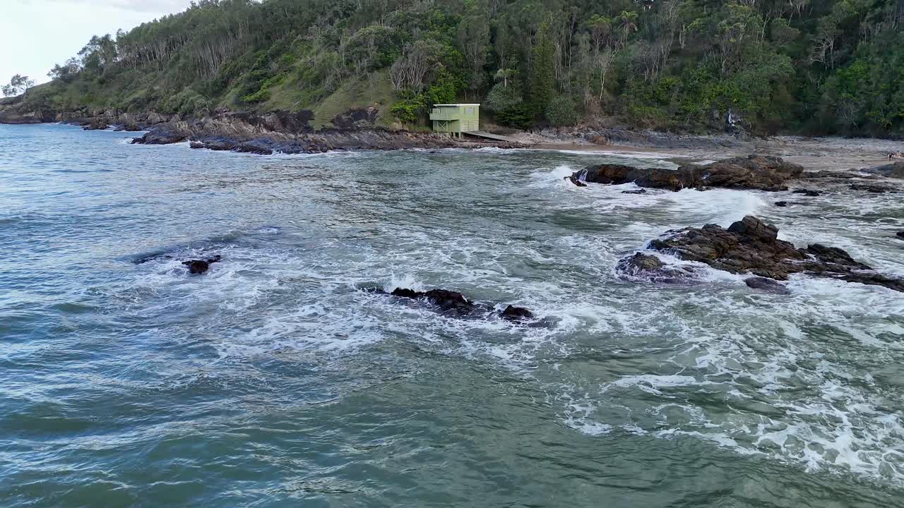 Aerial view of waves crashing against rocky shores at Charlesworth Bay Beach, under overcast skies, creating a serene coastal scene