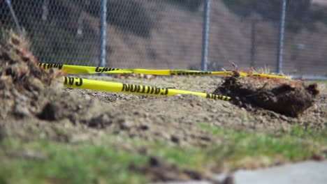 an empty desolate park enclosed by a chain link fence where the wind blows caution tape attached to a dirt rock