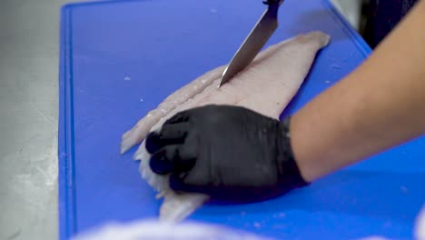 chef hands with black gloves cutting fish on a blue cutting board