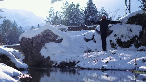 Woman-standing-next-to-a-lake-during-winter,-opening-arms-wide-to-the-side