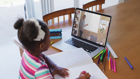 african american girl doing homework while having video call with male teacher on laptop at home