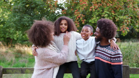 portrait of family on autumn walk in countryside standing by fence together