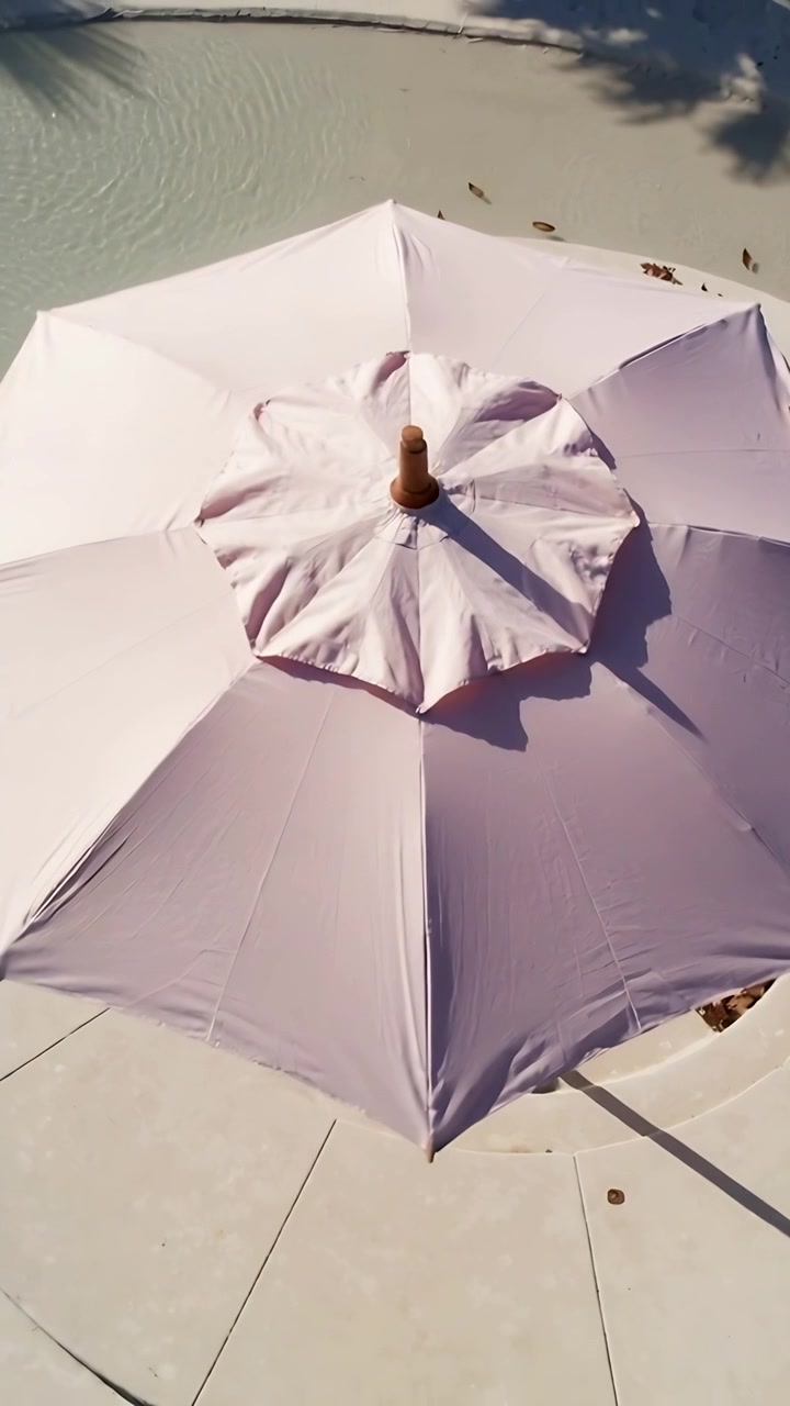 Video verticale: La telecamera panoramica rivela un ombrellone rosa che riempie l'inquadratura sul bordo piscina, mostrando il puntale.