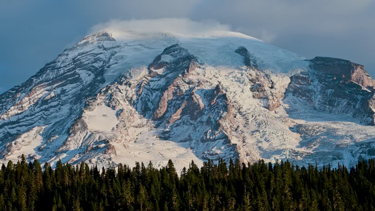 Majestic view of Mount Rainier rising above a dense evergreen forest under a moody sky, captured in stunning clarity