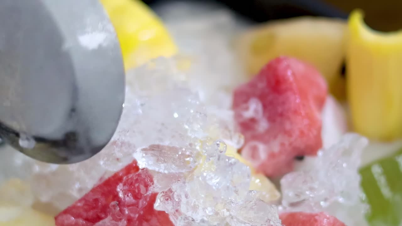 A close-up view of a vibrant fruit dessert with ice and a spoon.