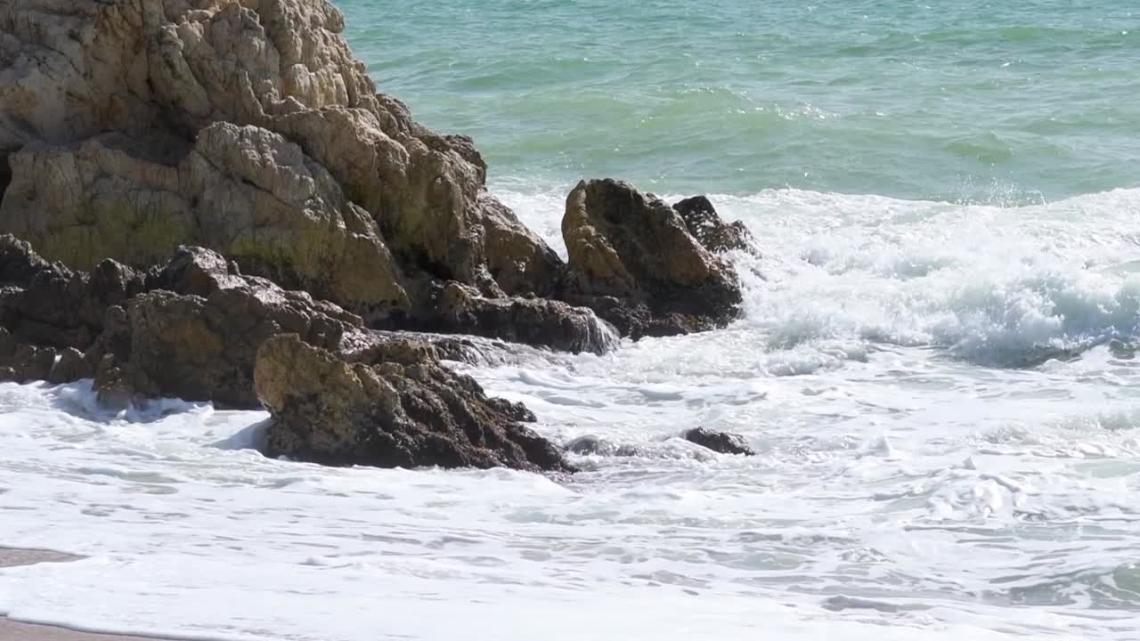 Mare agitato che si infrange sulle rocce mentre raggiunge la riva in una giornata di sole a mezzogiorno