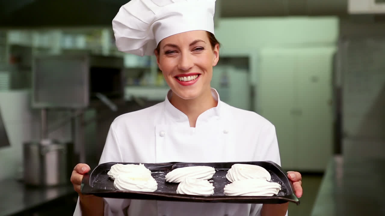 Chef felice che sorride alla telecamera mostrando un vassoio di meringhe