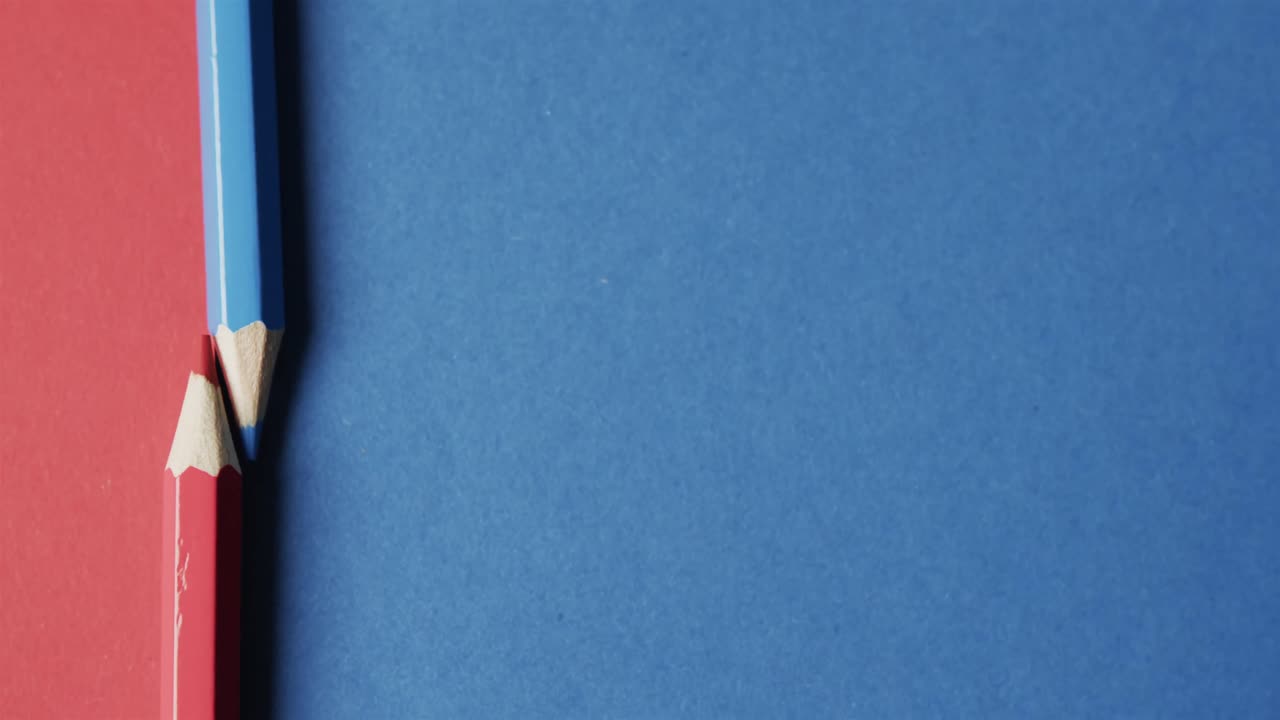 vista aérea de lápices de colores azules y rojos con espacio de copia en fondo rojo y azul, en cámara lenta