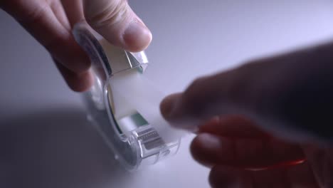 hands of a woman pulling tape from a transparent scotch tape dispenser