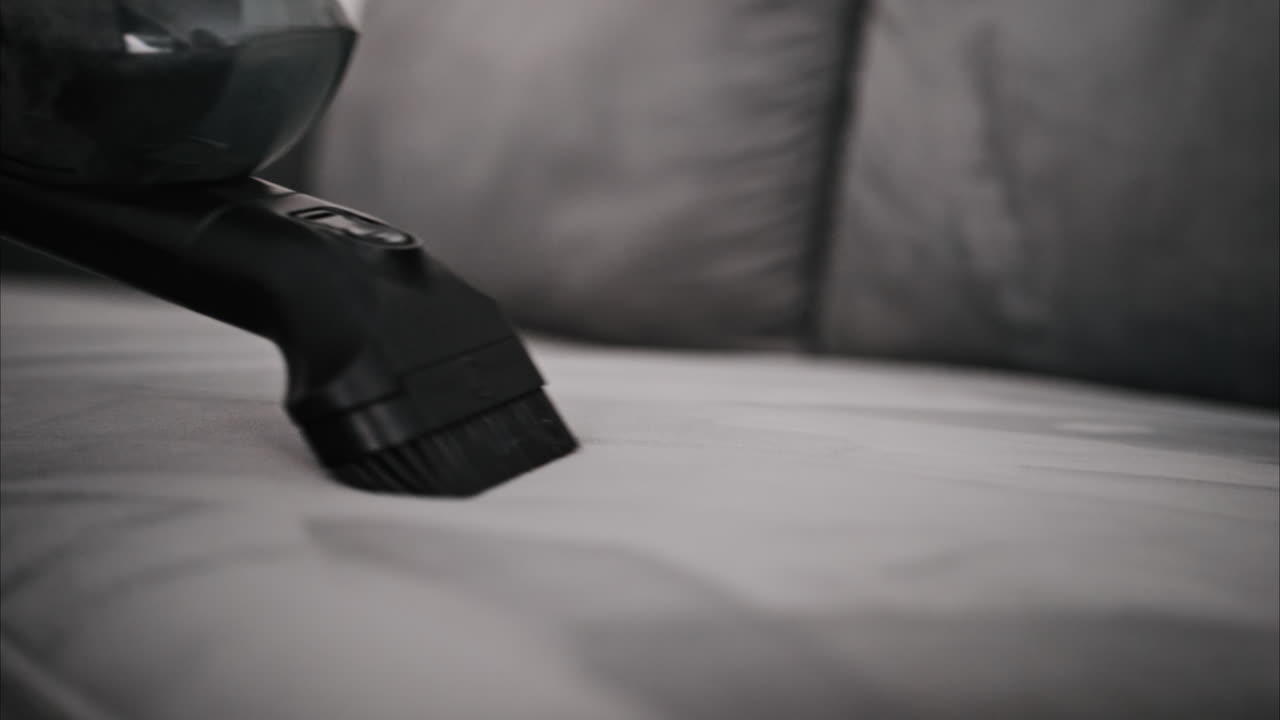 Close up of a small vacuum cleaning a grey couch