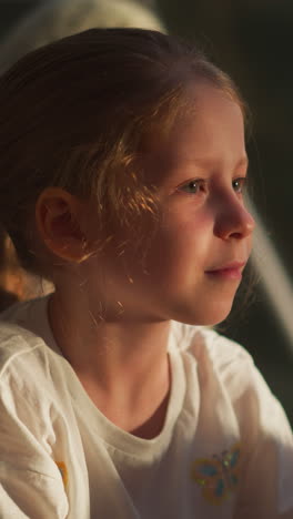 dreamy kid smiles peacefully. calm girl finds comfort in tranquil moment sitting near sunlit window in tent. cheerful kid at home in evening