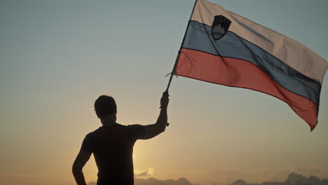 hiker standing in the early morning with a hiking pole in one hand on which a slovenina flag is attached