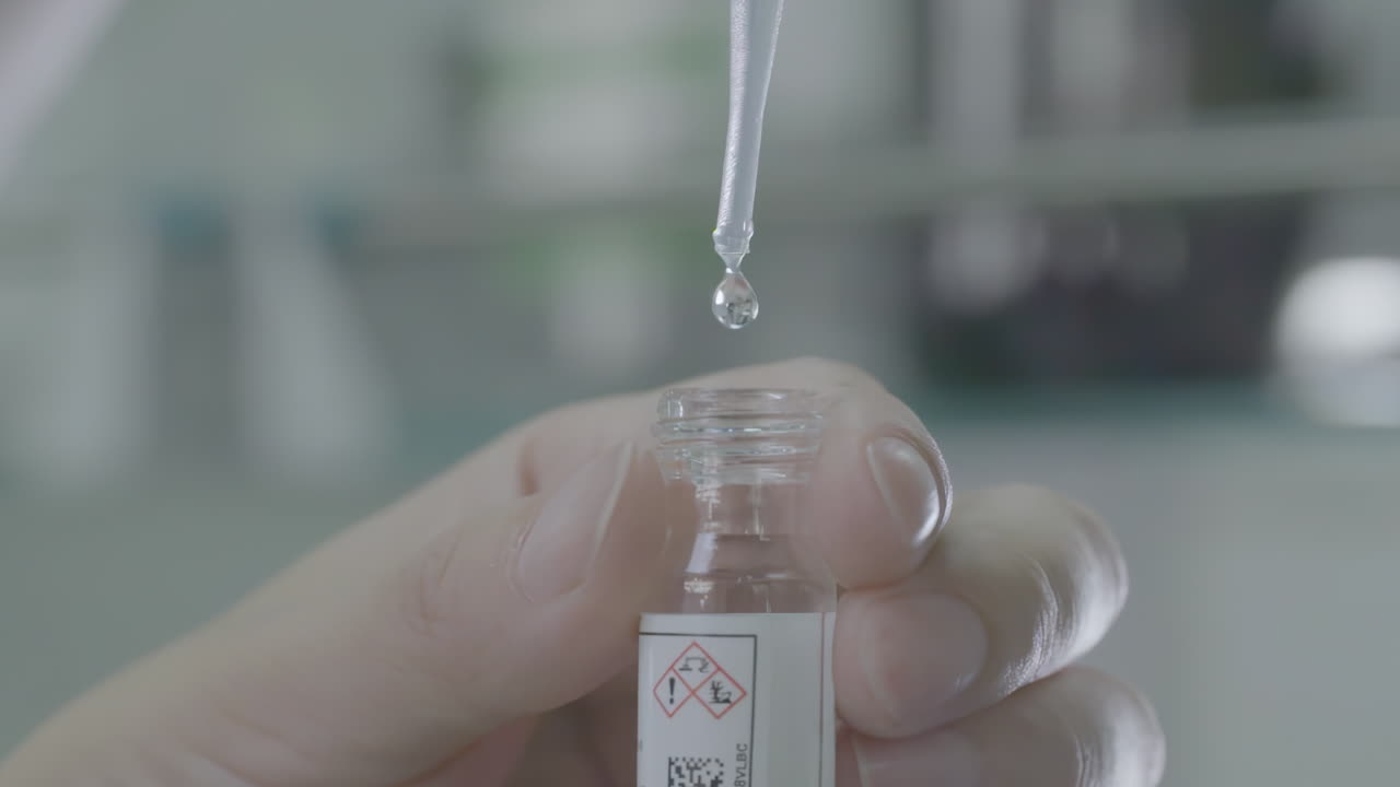 Close-up of a Hand Using a Pipette to Add a Drop of Liquid to a Small Vial in a Laboratory