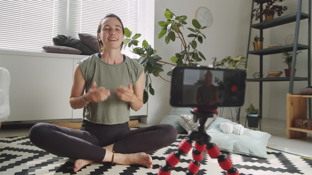 mujer alegre filmando un vlog de yoga con un teléfono inteligente en casa