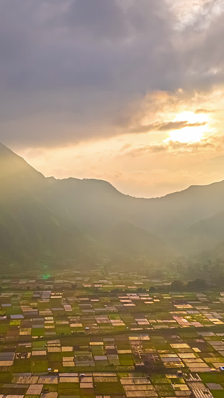 Aerial timelapse of fields in Bukit Selong valley at sunrise with hazy mountain backdrop