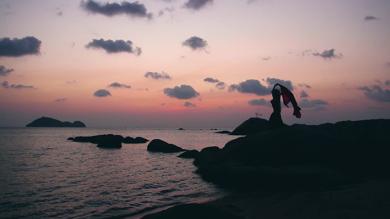Static footage of sexy, elegant and erotic arabian woman performing belly dance moves on the beach during golden hour. Silhouette.