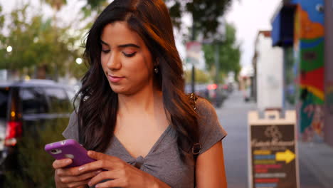 young woman texting on her phone on a city street at night