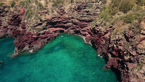 Drone-circles-small-shallow-water-bay-with-rock-walls-on-tropical-island-edge