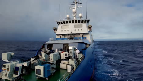 a research vessel with scientific equipment and crew on deck navigating the open ocean under an overcast sky