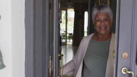 smiling senior mixed race woman opening front door and welcoming