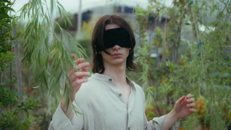 cinematic-middle-shot-of-young-man-walking-in-plant-nursery-with-blindfolded-eyes