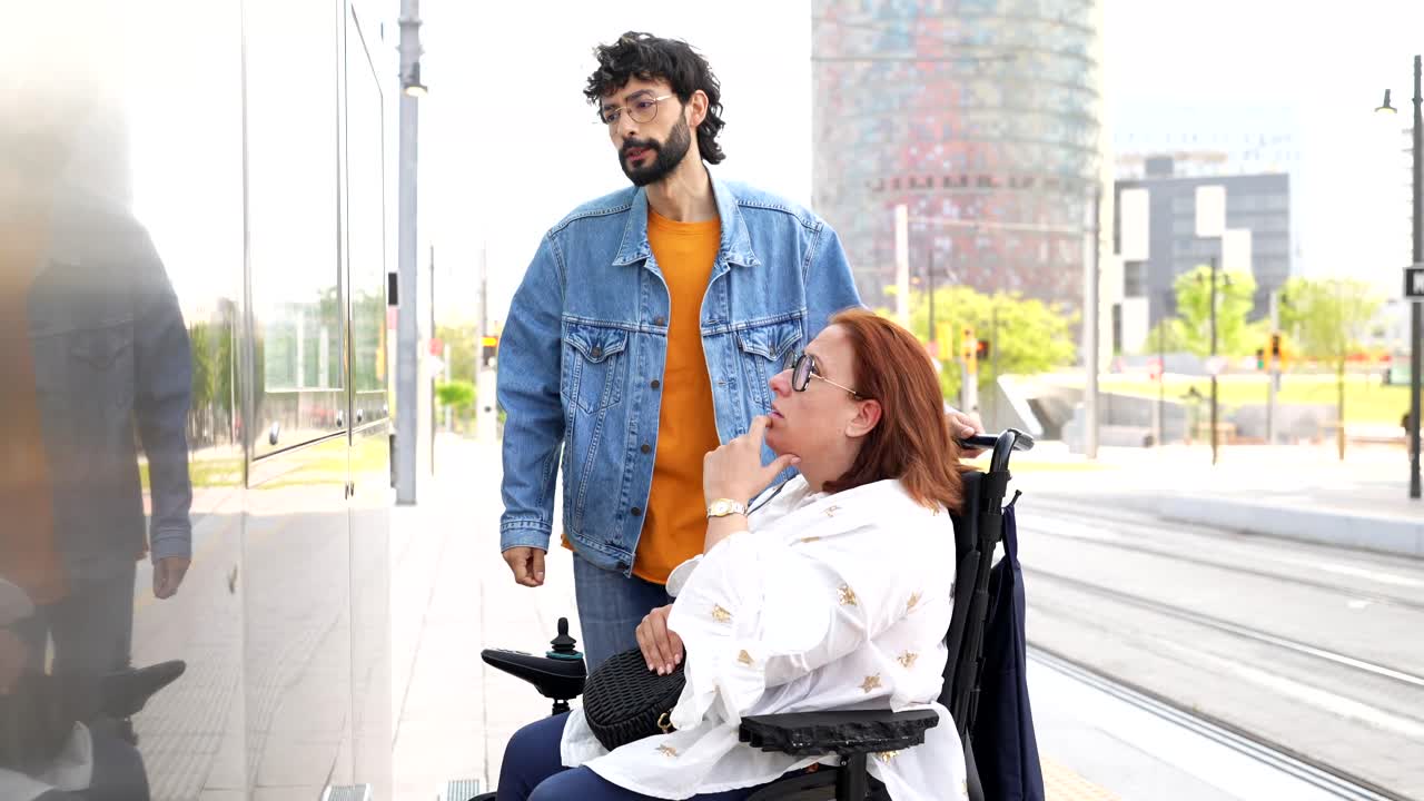 A man assisting a woman in a wheelchair at a public transport station