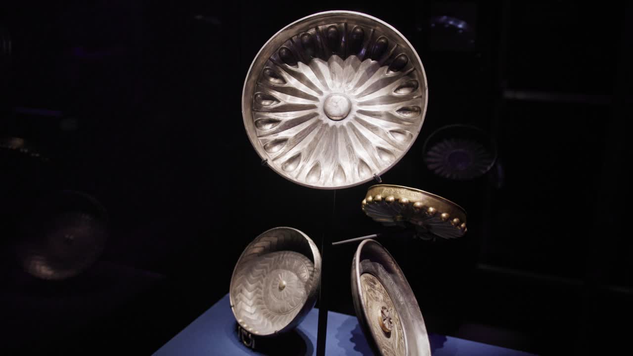 Samling af gamle egyptiske fajanceskåle med radiale og geometriske mønstre, udstillet i en mørk museumsudstilling med reflekterende glas og kurateret belysning.