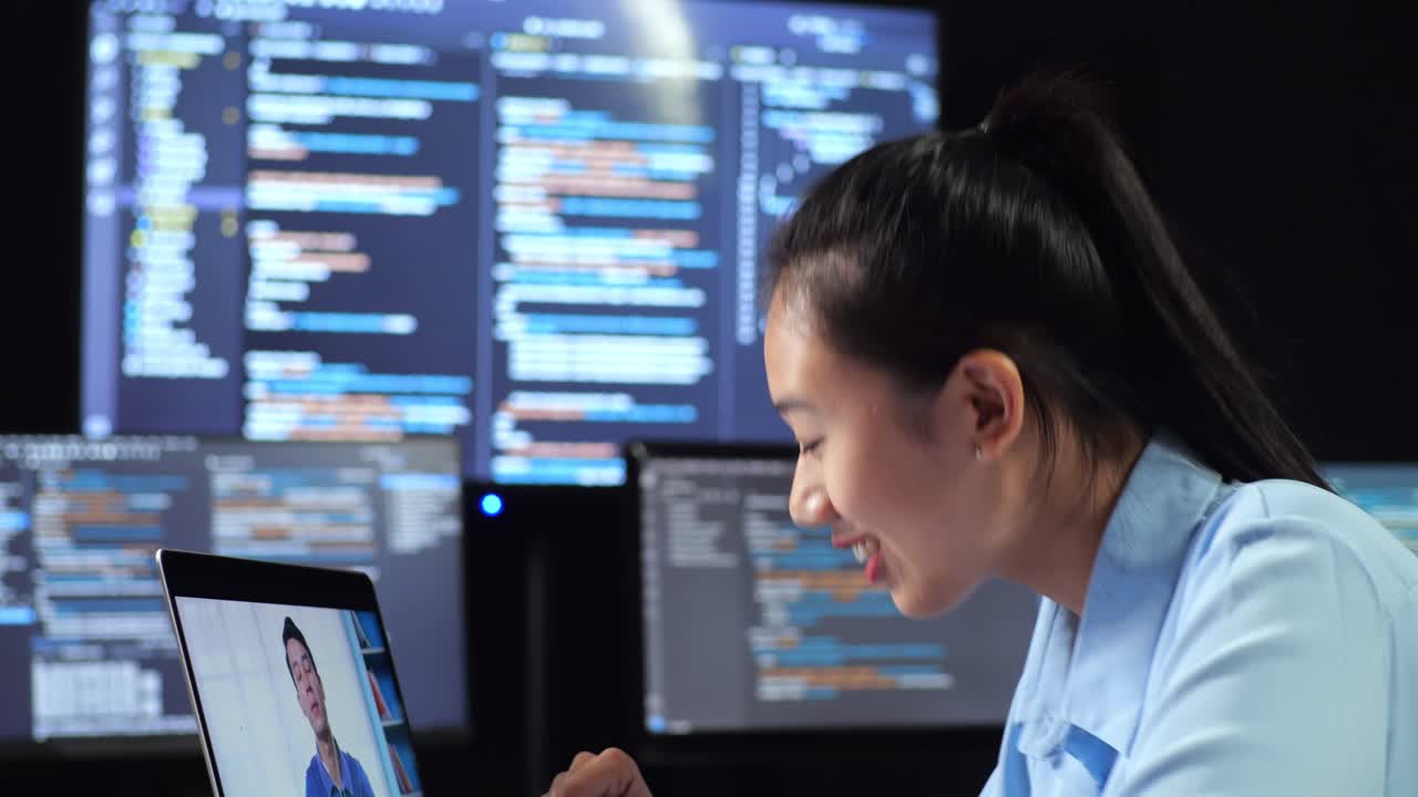 vista lateral de cerca de una programadora asiática teniendo una reunión con una computadora portátil mientras escribe código en múltiples monitores que muestra la base de datos en los escritorios de ventana de terminal en la oficina
