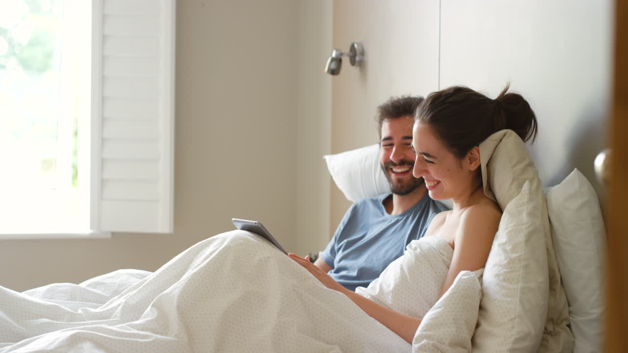 태블릿을 들고 침대에 누워있는 커플