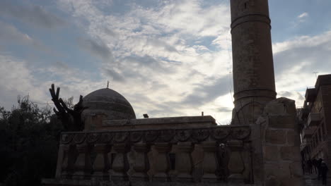 from the lower angle to the top, we see the silhouette of the mardin great mosque in the reverse light, and behind it the deep blue sky and the clouds that look like cotton