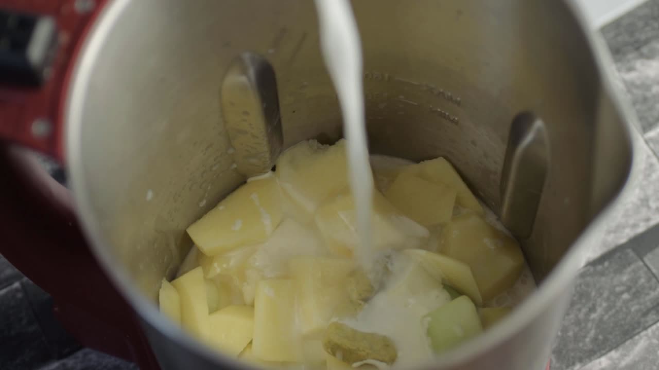Hand pouring liquid over ingredients in a soup maker close up shot