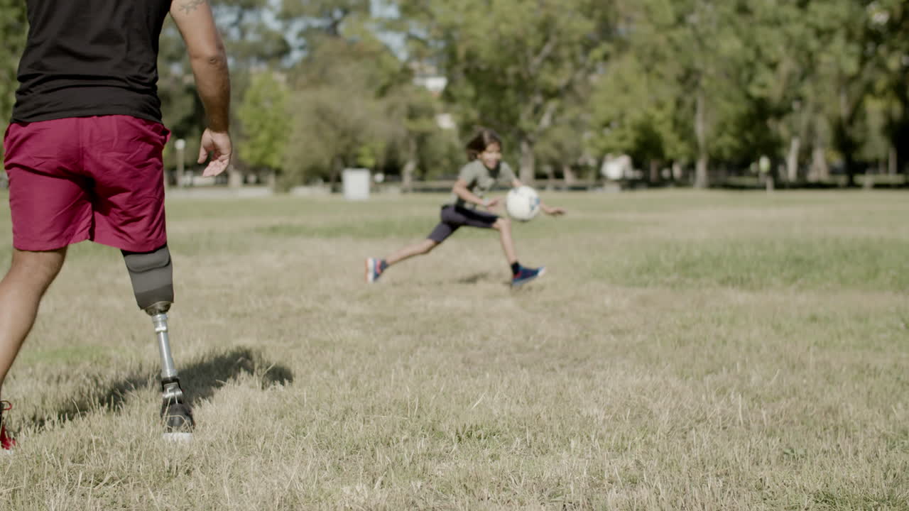 padre con mano artificial jugando al fútbol con su hijo en el césped