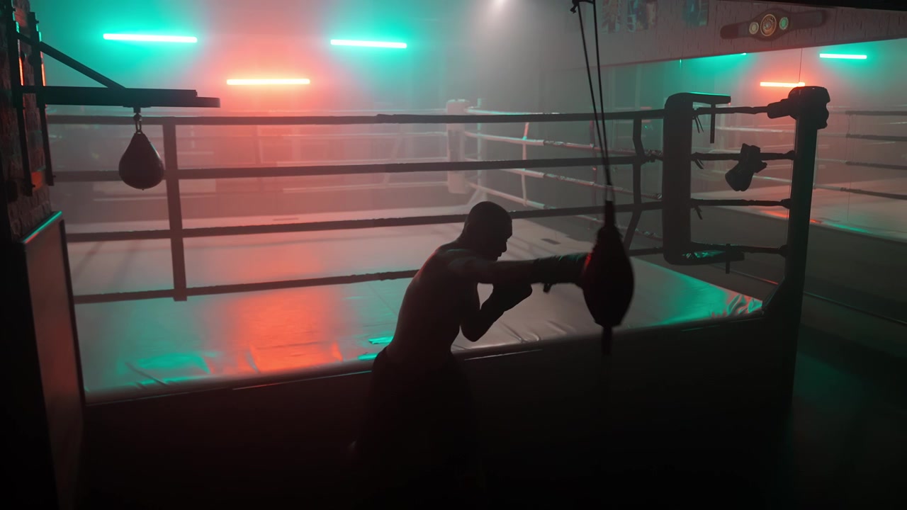 Silhuet af en bokser, der træner med en speedbag i et mørkt fitnesscenter