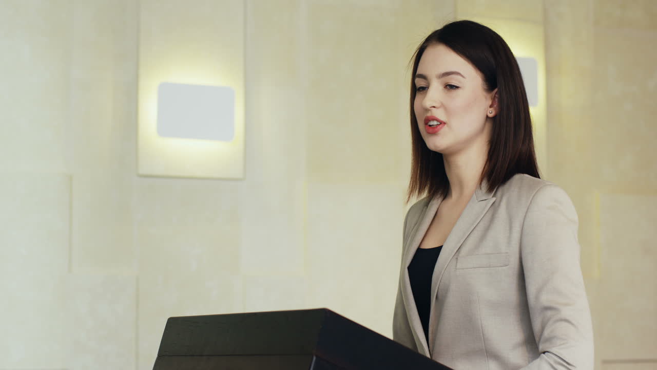 정장을 입고 회의실에서 많은 사람들 앞에서 이야기하는 연단에 있는 백인 여성 사업가의 클로즈업 보기